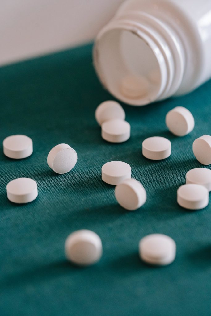 Closeup of spilled similar white round pills placed near plastic container on green surface